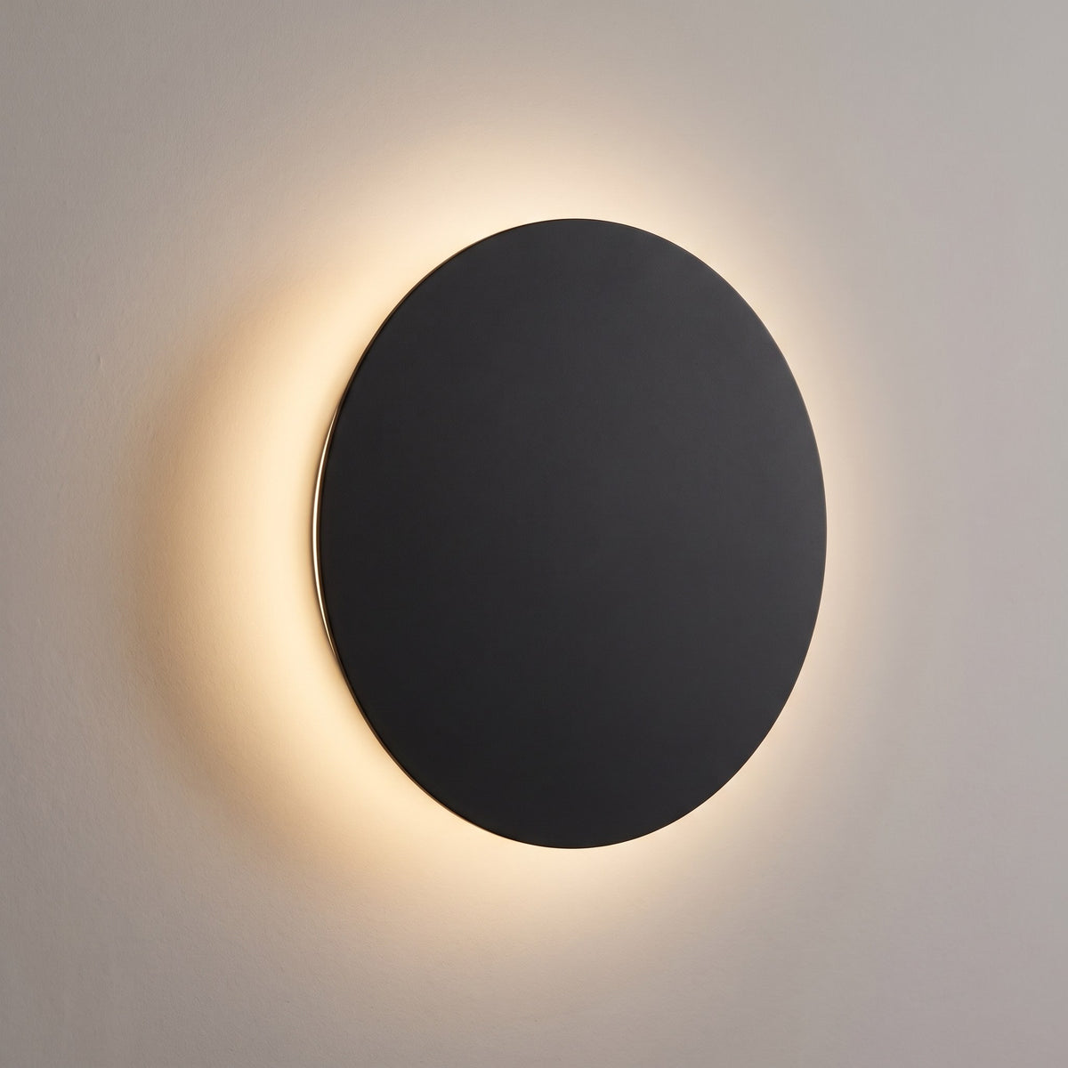 Rund LED-vägglampa i svart med varm halo på väggen – eclipse-design